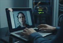 Écran d'ordinateur portable affichant un appel vidéo avec une image légèrement pixelisée, mains hésitantes sur le clavier