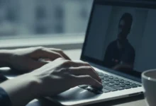 Mains sur un clavier d'ordinateur portable avec un appel vidéo flou en arrière-plan, lumière naturelle